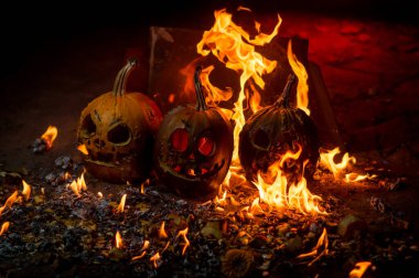 autumn holiday Halloween 2025 scary orange pumpkins burning in fire and smoke with blood red light in the dark