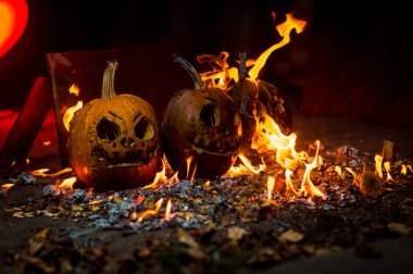 autumn holiday Halloween 2025 scary orange pumpkins burning in fire and smoke with blood red light in the dark