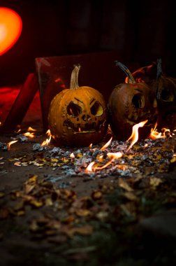 autumn holiday Halloween 2025 scary orange pumpkins burning in fire and smoke with blood red light in the dark