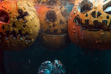 autumn holiday Halloween 2025 scary orange pumpkins drowning in water with bubbles and splatters in blood red light in the dark