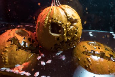 autumn holiday Halloween 2025 scary orange pumpkins drowning in water with bubbles and splatters in blood red light in the dark