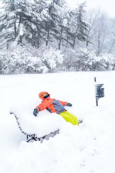 Маленький хлопчик лежить на лавці зі снігом. Вертикальний перегляд з дитиною i — стокове фото