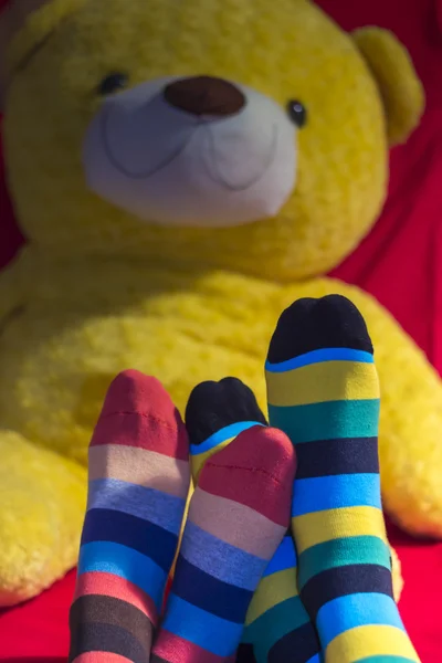 Färgade strumpor på tonåringar fötter över gul nallebjörn — Stockfoto