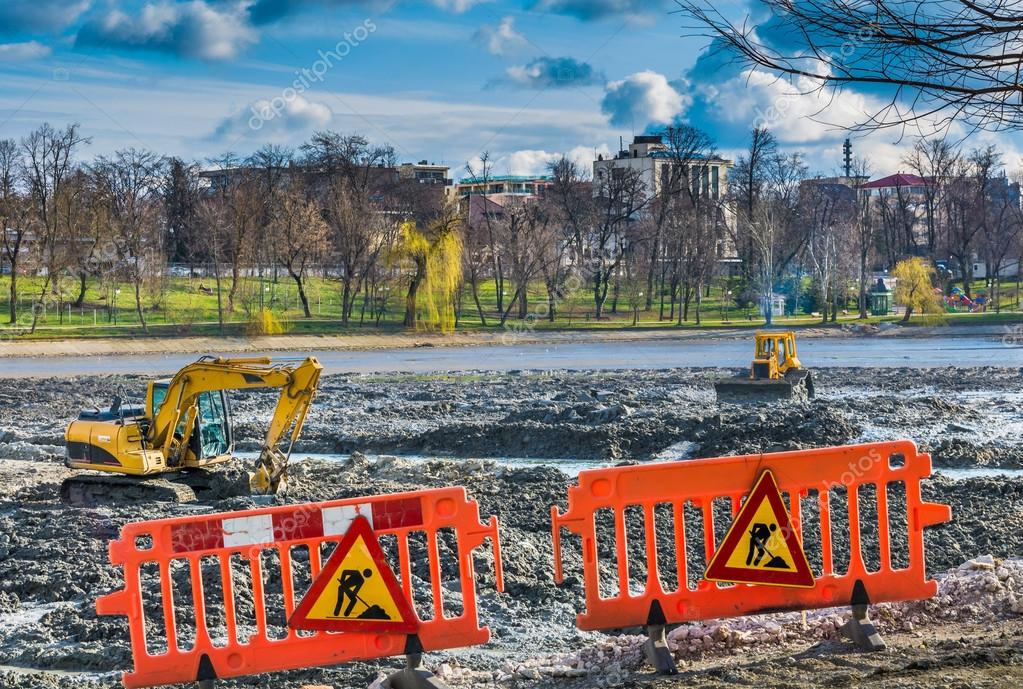 Yellow excavator doing lake cleaning and maintenance services under municipality authority in spring time in a park