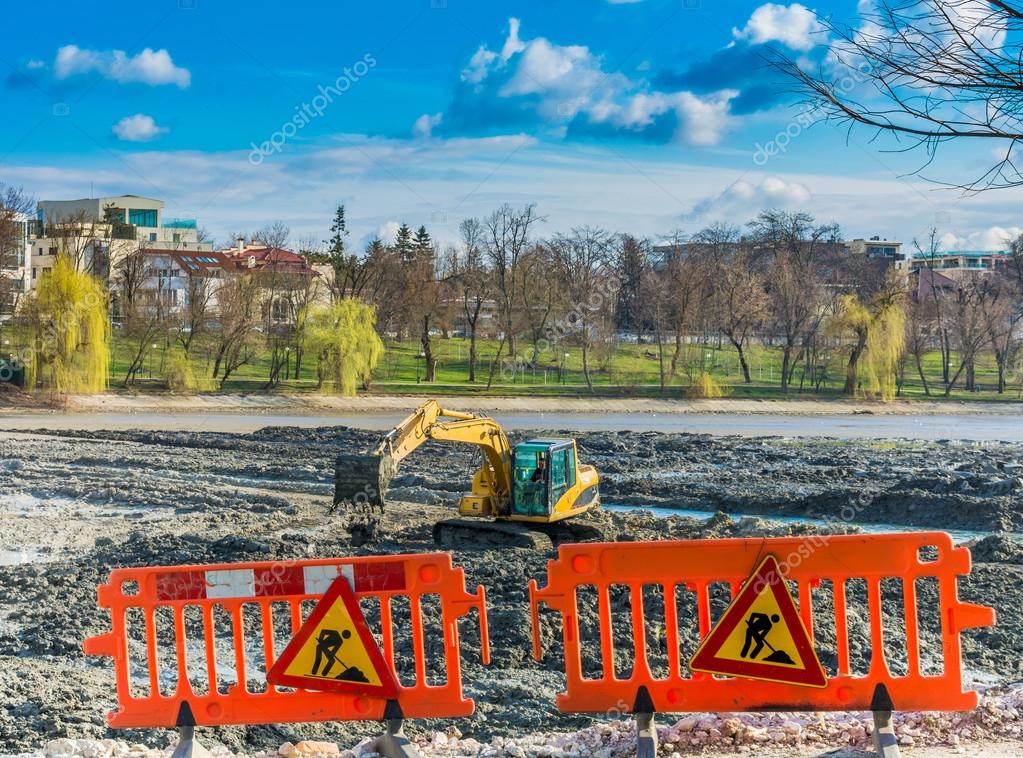 Yellow excavator doing lake cleaning and maintenance services under municipality authority  in a park