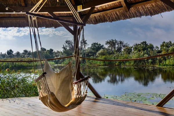 Sedia amaca nel pergolato sullo sfondo della natura. Vista tranquilla sul lago dal gazebo in legno . — Foto Stock