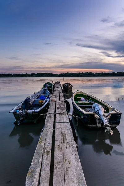 Quatre bateaux amarrés au coucher du soleil près d'une jetée en bois. Vue verticale de — Photo