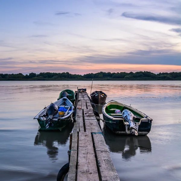 Four moored boats at sunset near a wooden pier. Vertical view of — Stock Photo, Image