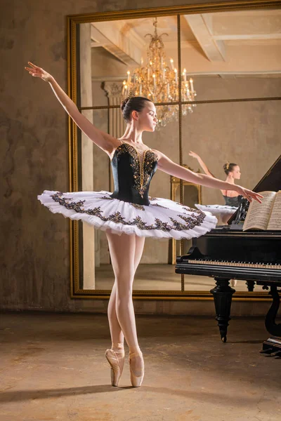 Young ballerina in a white tutu dancing on a beautiful old piano in a vintage interior