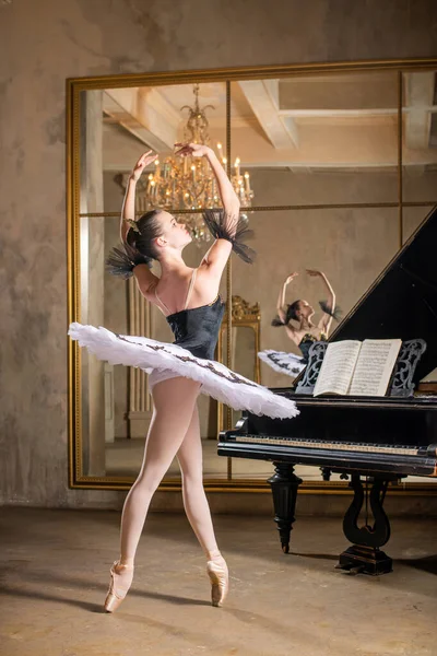 Young ballerina in a white tutu dancing on a beautiful old piano in a vintage interior