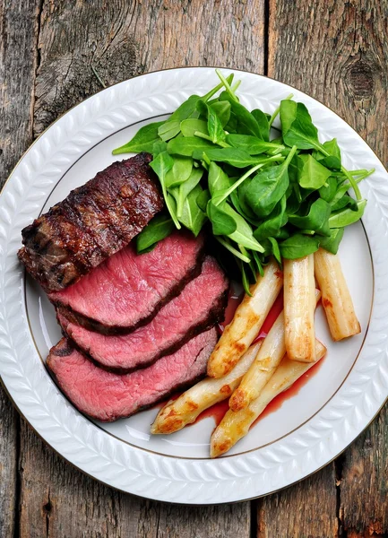Medium rare steak with asparagus and baby spinach. — Stock Photo, Image