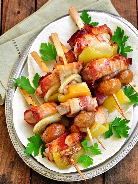 Porc enveloppé dans du bacon sur des brochettes grillées aux oignons, champignons et poivrons . — Photo