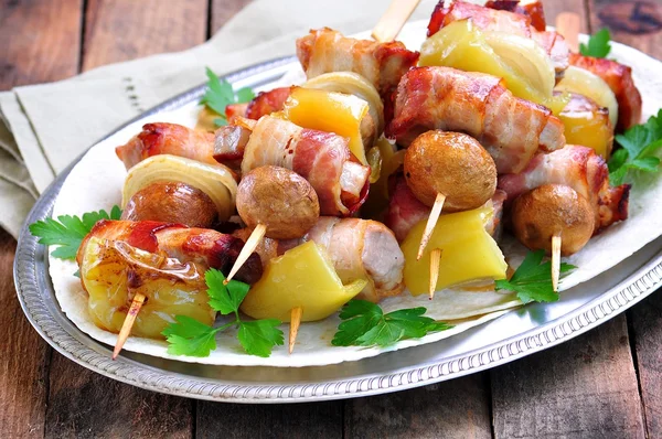 Pork wrapped in bacon on skewers grilled with onions, mushrooms and peppers. — Stock Photo, Image