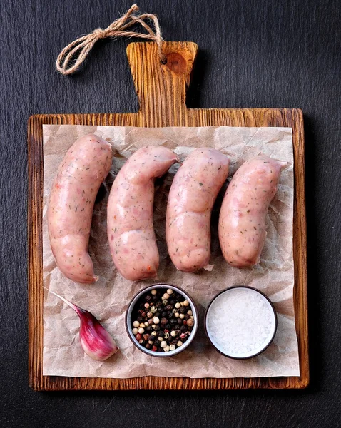 Embutidos de pollo crudo con ajo y perejil en una tabla de cortar de madera — Foto de Stock