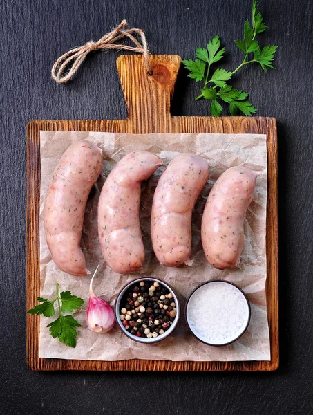 Сырые куриные сосиски с чесноком и петрушкой на деревянной доске — стоковое фото