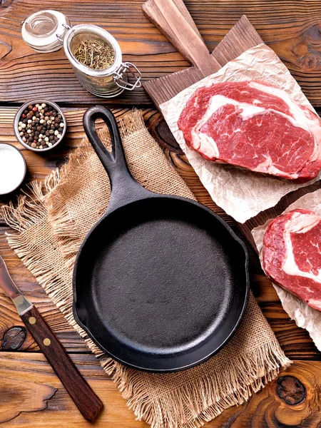 Casserole en fonte avec steak de côtelette cru sur fond en bois . — Photo