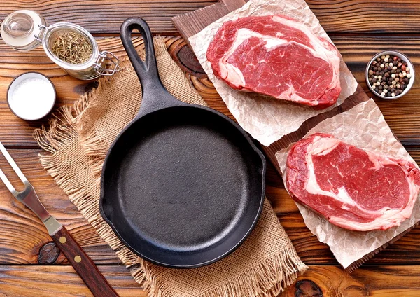 Casserole en fonte avec steak de côtelette cru sur fond en bois . — Photo