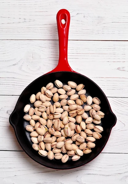 Roasted Pistachio nuts in a cast iron skillet on a white wooden background. — Stock Photo, Image