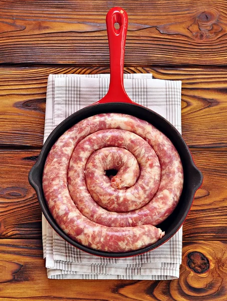 Raw pork sausage in a cast iron frying pan on a wooden background. — Stock Photo, Image