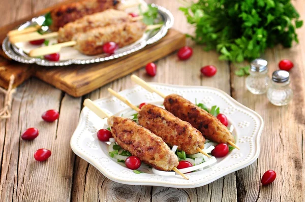 Homemade meat kebabs skewers with dogberry and onion salad on wooden background. — Stock Photo, Image