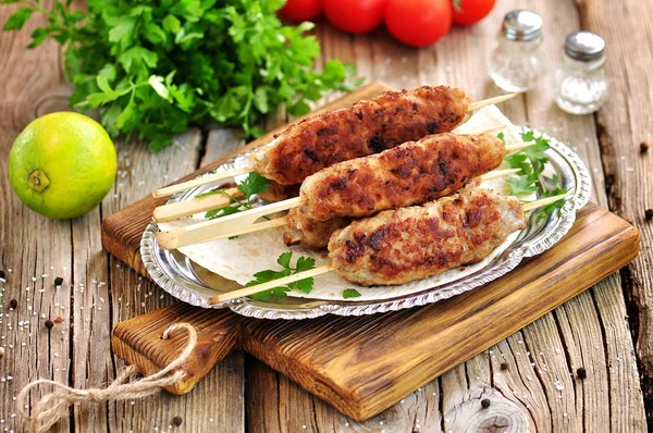 Homemade meat kebabs skewers with dogberry and onion salad on wooden background. — Stock Photo, Image