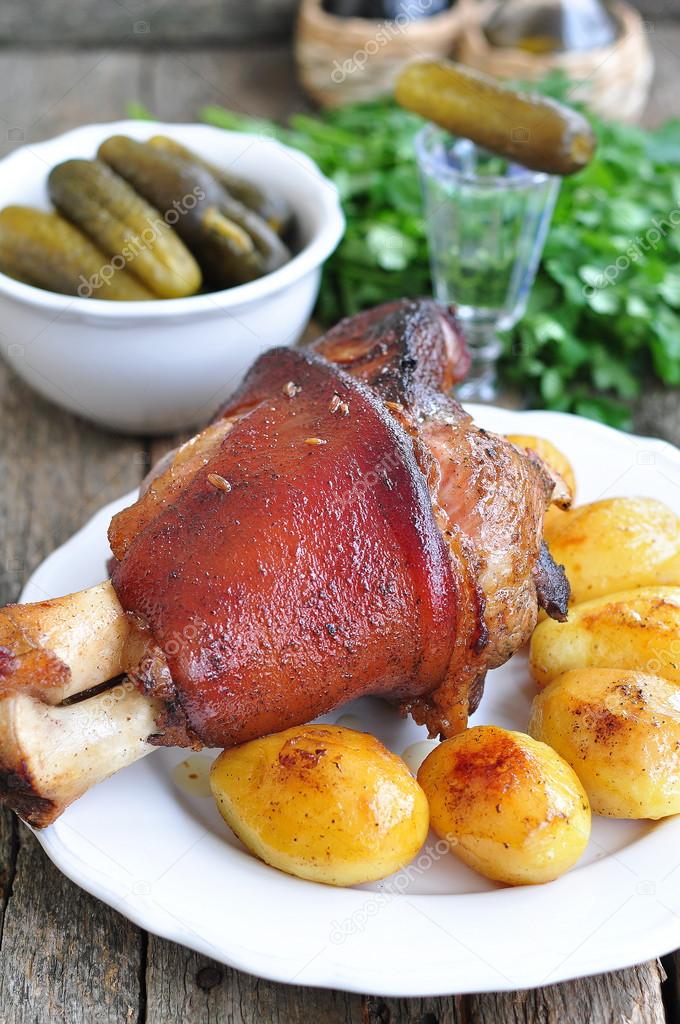 Appetizing Bavarian roast pork knuckle on cutting board with the baked potato
