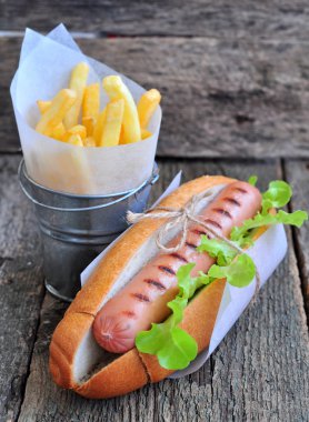 Sosisli sandviç taze marul ve ahşap bir masa üzerinde patates kızartması ile