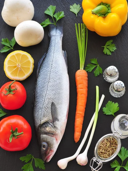 Roher Fisch mit frischem Gemüse auf schwarzem Hintergrund — Stockfoto