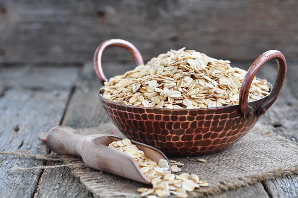 Oat flakes in a copper plate on a wooden table — 스톡 사진