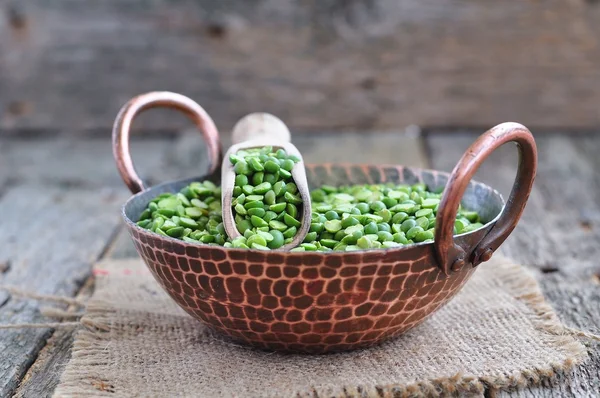 Dried green split peas in a copper plate on a wooden table — Stock Fotó