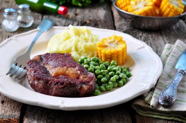 Rare beef steak with mashed potatoes, green peas and boiled corn