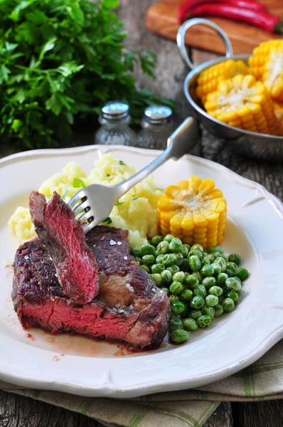 Rare beef steak with mashed potatoes, green peas and boiled corn — Stock Photo, Image