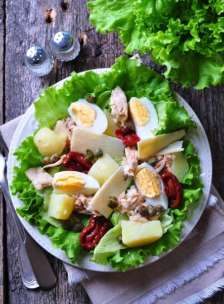 salad of lettuce, iceberg lettuce, with canned tuna, dried tomatoes, boiled potatoes, capers and parmesan cheese, dressed with olive oil. Selective focus. rustic style.