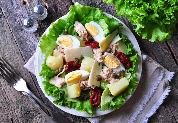 Salad of lettuce, iceberg lettuce, with canned tuna, dried tomatoes, boiled potatoes, capers and parmesan cheese, dressed with olive oil. Selective focus. rustic style. — Stock Photo, Image
