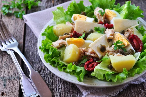 Ensalada de lechuga, lechuga iceberg, con atún enlatado, tomates secos, patatas hervidas, alcaparras y queso parmesano, aderezado con aceite de oliva. Enfoque selectivo. estilo rústico . — Foto de Stock