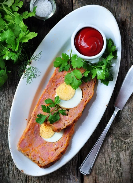 Meat loaf with boiled egg, tomato sauce, coriander and parsley on a wooden table. rustic style. — Stock Photo, Image