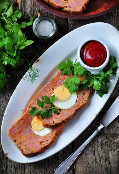 Meat loaf with boiled egg, tomato sauce, coriander and parsley on a wooden table. rustic style. — Stock Photo, Image