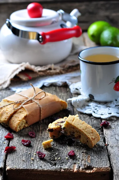 Homemade biscotti with dried cranberries and lime, with a cup of green tea kettle on the wooden table. rustic style. — Stok fotoğraf