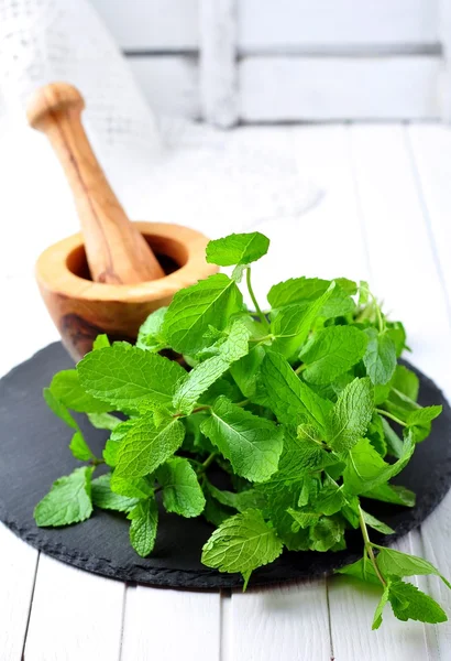 Organic mint and wooden mortar with pestle of olive on a black stone — Zdjęcie stockowe