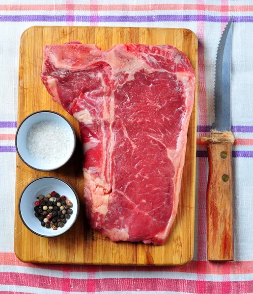 Bife suculento cru de carne de T-Bone em uma placa de madeira com sal, pimenta e uma faca — Fotografia de Stock