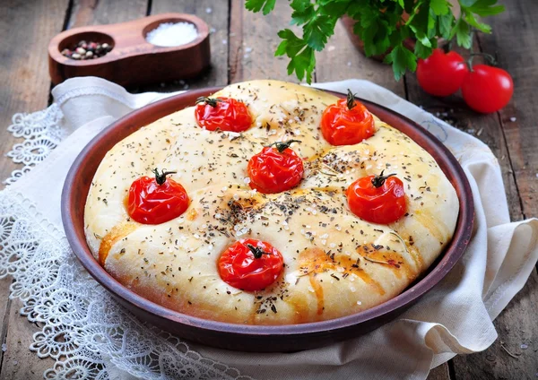 Homemade focaccia with cherry tomatoes, sea salt and herbs in a clay bowl on a gray wooden background. — Stock Photo, Image