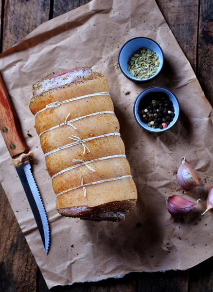 Nyers tekercs marinált sertésborda belly édeskömény, szárított bazsalikom, rozmaring, egy fából készült asztal. — Stock Fotó