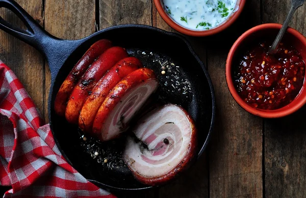 Roast pork belly roll with pepper, sea salt, dried rosemary, basil and garlic on a wooden table. Rustic style. Selective focus. — Stock Image Roast pork belly roll with pepper, sea salt, dried rosemary, basil and garlic on a wooden table. Rustic style. Selective focus. Stock Picture