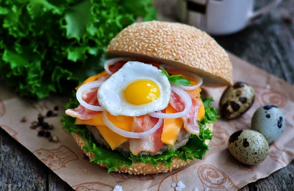 homemade burger with beef, bacon, cheese, onion, lettuce and quail egg