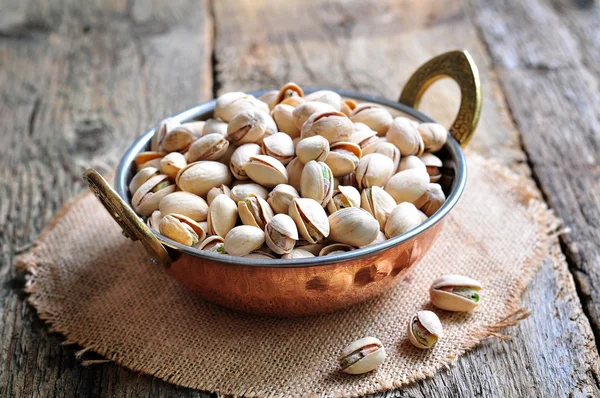 Pistachio in a copper bowl on the old wooden background — Stock Photo, Image