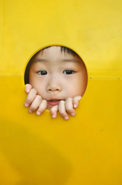 Asiatique fille bâtons visage à travers un trou dans aire de jeux — Photo