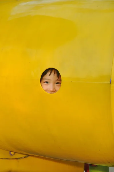 Asain chica mira a través de agujero en el patio de recreo —  Fotos de Stock