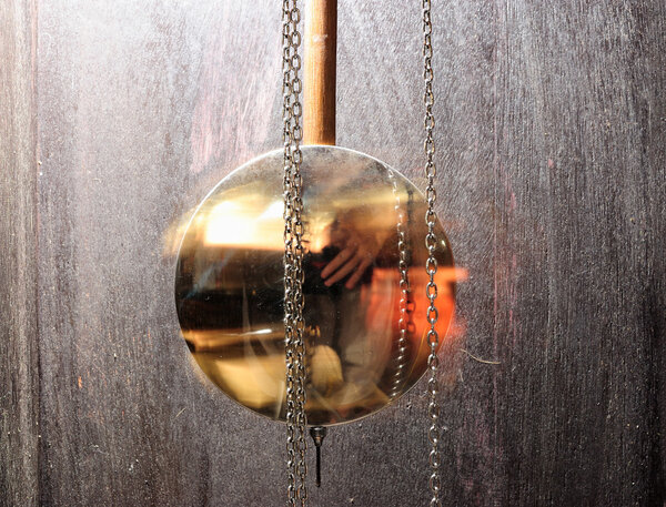 металлические маятниковые часы, качающиеся на деревянном фоне
