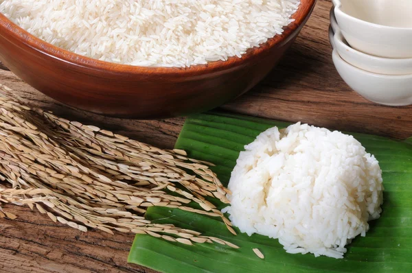 Gekookte rijst, ongekookte rijst en padie op houten tafel — Stockfoto