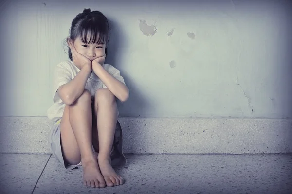 Сумна і пригнічена маленька дівчинка, що сидить біля стіни — стокове фото